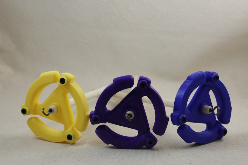 May include: Three spinning wheels for yarn, one yellow, one purple, and one blue. Each wheel has a three-pronged design and a small hook in the center.
