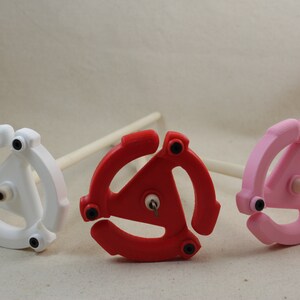 May include: Three spinning wheels with different colored bases: white, red, and pink. Each wheel has a triangular shape with three arms and a small hook in the center.