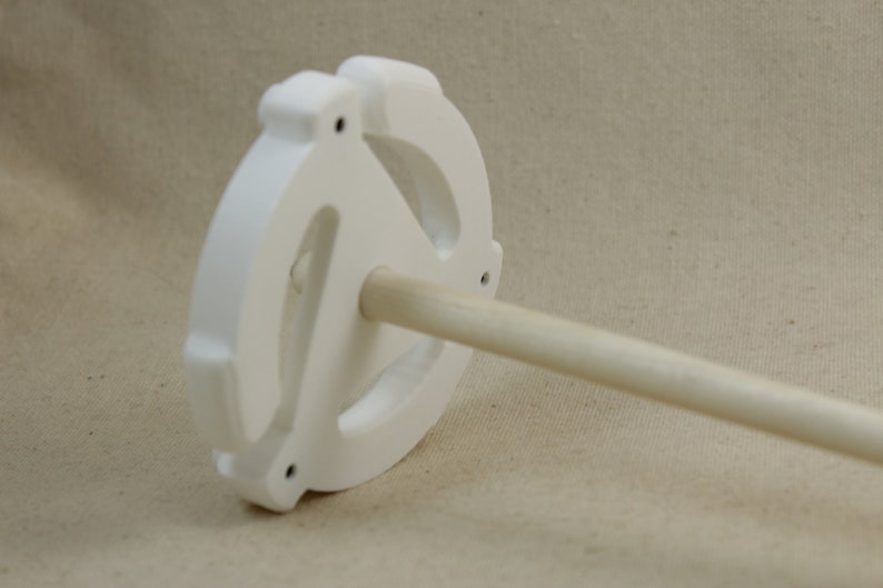 May include: White ceramic spinning wheel with a wooden spindle. The wheel has a unique design with three holes.