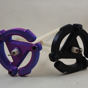 May include: Two spinning wheels, one purple and one black, with a wooden spindle. The wheels are shaped like a record with a triangular center.