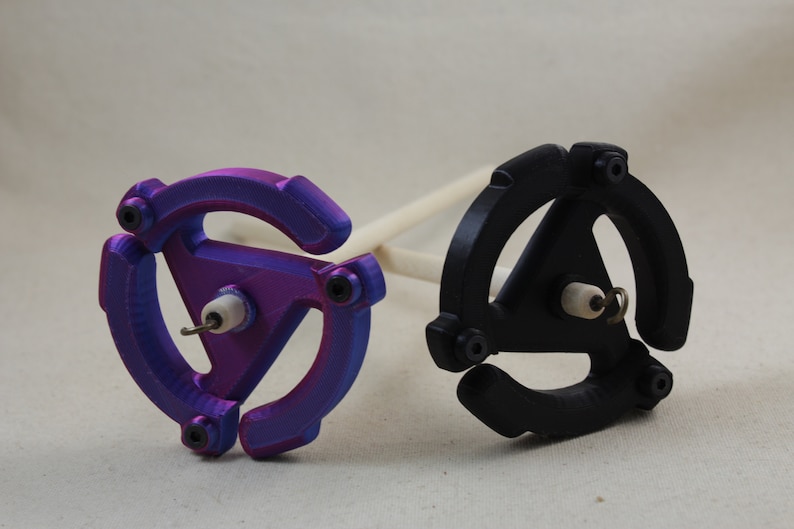 May include: Two spinning wheels, one purple and one black, with a wooden spindle. The wheels are shaped like a record with a triangular center.