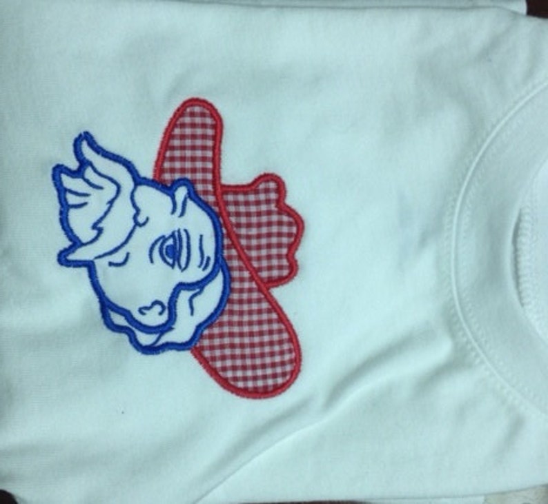 May include: White t-shirt with an embroidered red and white gingham cowboy hat and blue cartoon face.