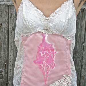 May include: A white lace top with a pink fabric panel featuring a floral design. The top has a sweetheart neckline and adjustable straps.