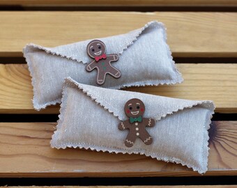Könnte beinhalten: Zwei kleine Leinentaschen mit Lebkuchenmann-Dekorationen. Die Taschen sind beige mit einem gewellten Rand und liegen auf einer Holzoberfläche.