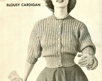 May include: A gray knitted cardigan with a button-up front and a blousy fit. The cardigan is worn by a woman with a pearl necklace and a skirt.