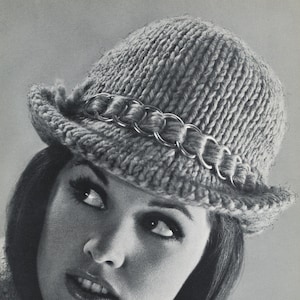 May include: A woman wearing a gray knitted hat with a silver chain detail. The hat has a wide brim and is pulled down over her forehead.