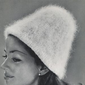Puede incluir: Una mujer con un gorro de punto blanco y peludo. El gorro está tirado hacia abajo sobre su frente y le cubre las orejas. Su cabello es oscuro y está peinado en una suave onda.