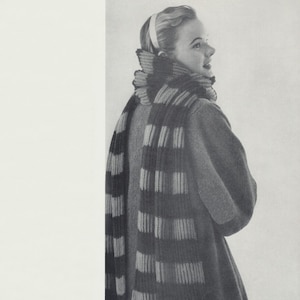 May include: A woman wearing a grey coat with a black and grey striped scarf. The scarf is wrapped around her neck and tied in a loose knot.