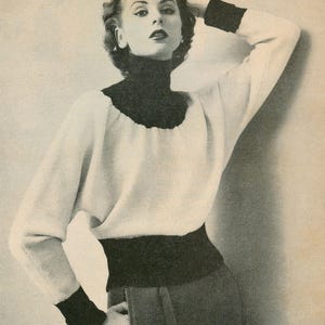 May include: A vintage black and white photograph of a woman wearing a white sweater with a black turtleneck, cuffs, and waistband. The woman is posing with one arm raised, and her other hand is in her pocket. The sweater has a relaxed fit.
