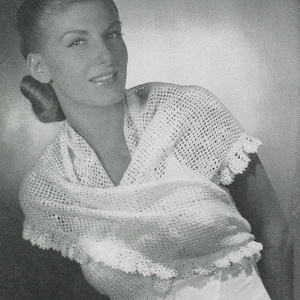 Puede incluir: Una mujer lleva una chal de ganchillo blanco con un delicado borde de encaje. El chal está drapeado sobre sus hombros y está atado al cuello.