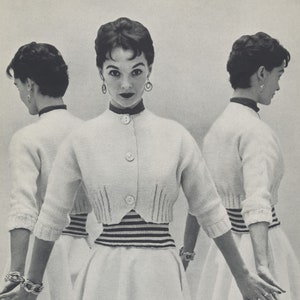 May include: A woman wearing a white cropped cardigan with a black and white striped band around the waist. She is wearing a white skirt and has her hair styled in a short, neat bob.