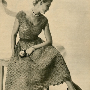 Könnte beinhalten: Eine Frau in einem zarten, spitzen Kleid mit einer Perlenkette und einer kleinen Blume in der Hand. Sie sitzt auf einem Holzhocker mit gekreuzten Beinen und trägt schwarze Schuhe mit Absatz.