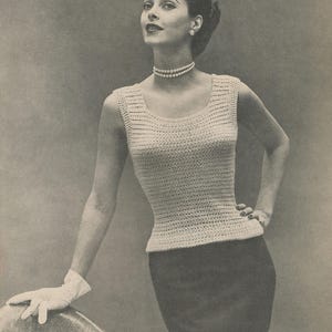 Op de afbeelding: Een vintage afbeelding van een vrouw in een crèmekleurige, mouwloze gehaakte top en een donkere rok. Ze draagt een parelketting en oorbellen. De top heeft een getailleerd silhouet.