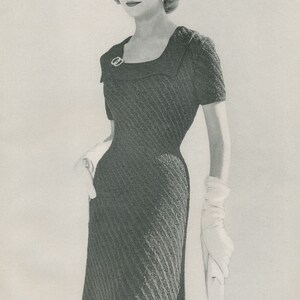 May include: A black and white photo of a woman wearing a fitted, textured, black dress with a square neckline and short sleeves. She is wearing white gloves and has her hair styled in a short, neat updo.