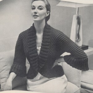 May include: A black knitted cardigan with a wide collar and bell sleeves. The cardigan is cropped and has a relaxed fit.