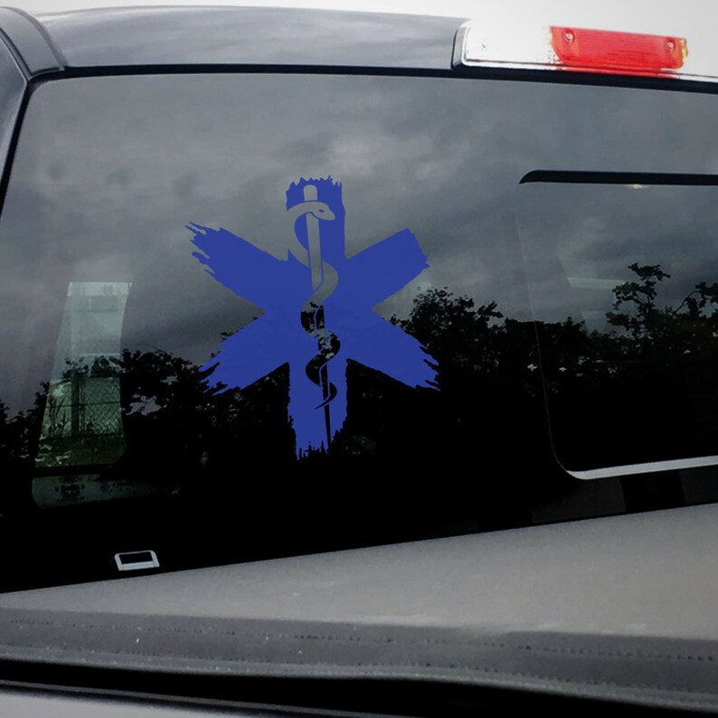 Op de afbeelding: Een blauwe en witte medische symboolsticker met een slang die om een ​​staf is gewikkeld. Het symbool bevindt zich op de achterruit van een zwarte vrachtwagen.