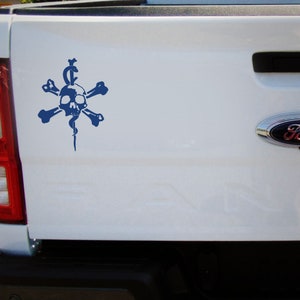Puede incluir: Una pegatina azul de calavera y huesos cruzados con una serpiente envuelta alrededor de un bast&oacute;n, en la parte trasera de una camioneta blanca.