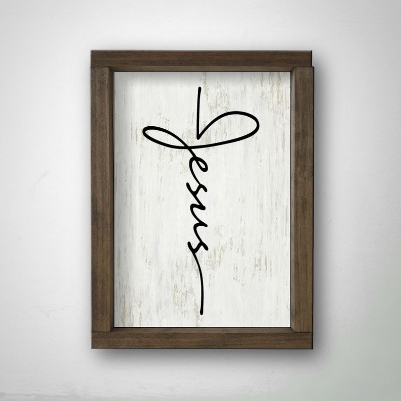 May include: A framed wood sign with a white background and a black cursive inscription of "Jesus" in the shape of a cross.
