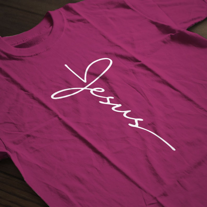 May include: A magenta t-shirt with the word "Jesus" written in white cursive script.