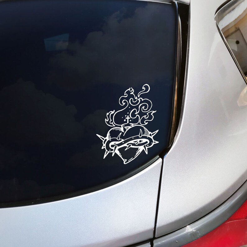 May include: A white vinyl sticker of a heart with thorns and flames on a silver car.