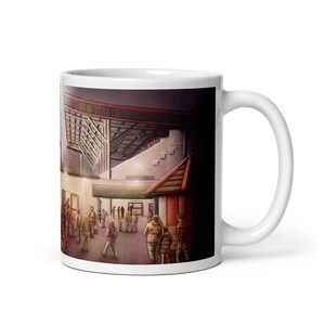 May include: White ceramic mug featuring an illustration of a stadium exterior with people. The artwork depicts a crowd of people near a building with a red roof, and a stadium in the background.