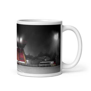 May include: White ceramic mug featuring a stadium scene at night. The image shows a stadium with red seating, bright lights, and a dark sky. The mug is a standard size, perfect for coffee or tea.