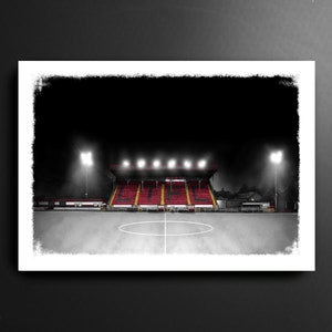 May include: A black and white illustration of a football stadium at night with floodlights illuminating the red and yellow seats. The stadium is empty and the field is covered in a light dusting of snow.