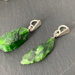 May include: A pair of earrings with green crystal pendants attached to silver jump rings.