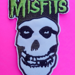 Op de afbeelding: Een geborduurde zwarte en witte patch met een schedel en het woord "MISFITS" in groene letters.