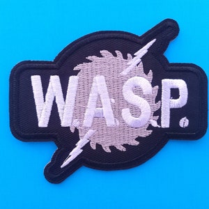 May include: Embroidered patch in black and white, featuring the letters "W.A.S.P." in white. The design includes a saw blade and lightning bolt. The patch has a black border and is set against a bright blue background.