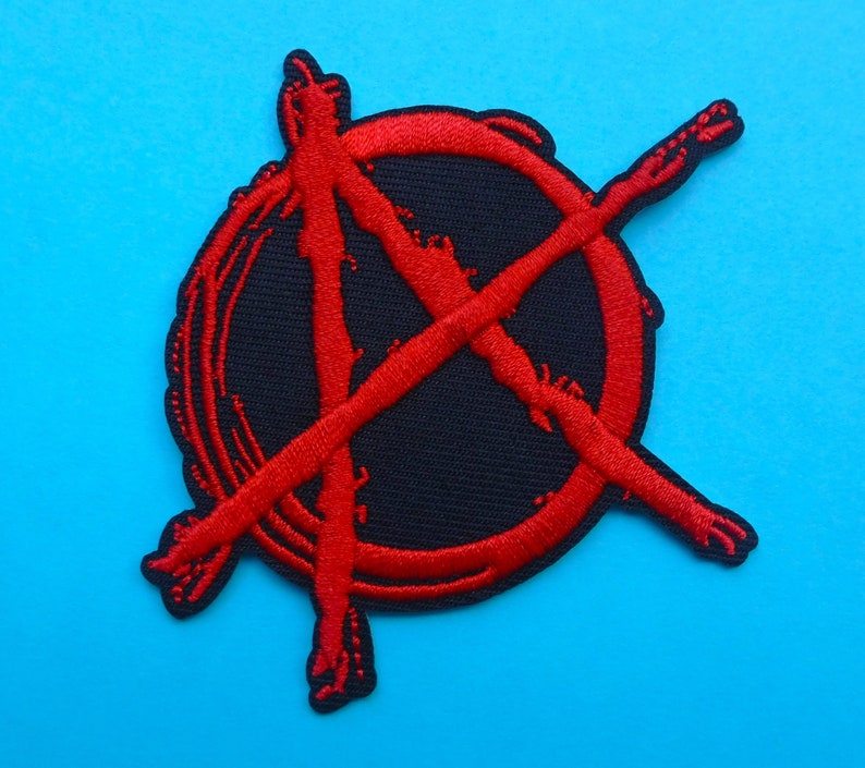 May include: A black patch with a red anarchy symbol. The symbol is a circle with a capital A and crossed lines, embroidered in red thread. The patch is set against a bright blue background. The patch is a circular shape.