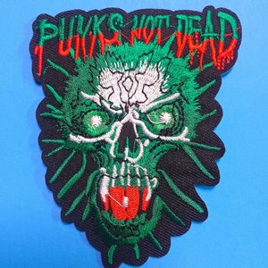 Op de afbeelding: Geborduurde patch met een schedelontwerp in groen, wit en rood. De patch heeft de tekst "Punks Not Dead" in het rood, met een zwarte rand en achtergrond. De schedel heeft groene ogen en een rode tong.