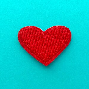 May include: A bright red heart-shaped patch with a textured surface, set against a vibrant teal background. The patch is likely made of fabric and has a stitched border, creating a distinct outline. Ideal for crafts or embellishments.