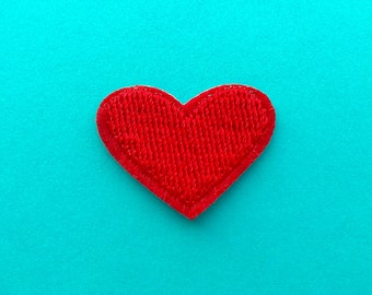 Könnte beinhalten: Ein leuchtend rotes herzförmiges Stoff-Patch mit strukturierter Oberfläche, vor einem türkisfarbenen Hintergrund. Der Patch hat einen genähten Rand, der eine deutliche Kontur erzeugt. Ideal für Bastelarbeiten oder Verzierungen.