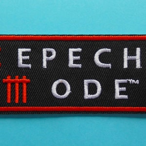 Puede incluir: Parche bordado con el texto "EPECHE MODE" en blanco, delineado en rojo sobre fondo negro. El parche tiene un borde rojo y dos símbolos rojos. El parche es rectangular.
