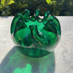 May include: A vibrant green glass bowl with a ruffled rim. The bowl is round with a glossy finish, casting a shadow on the surface below. The bowl's design is reminiscent of a flower.