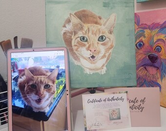 Peut inclure: Une tablette numérique affichant une photo d'un chat roux la bouche ouverte, à côté d'une peinture d'un chat roux sur toile, et un certificat d'authenticité pour la peinture.