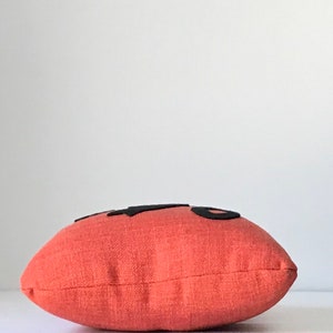 May include: A coral-colored pillow with black felt lettering that reads "Hello".