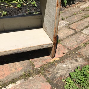 Pode incluir: Uma estante de madeira com acabamento pintado de branco. A estante &eacute; feita de madeira bruta e tem um visual r&uacute;stico. A estante est&aacute; sentada em um p&aacute;tio de tijolos.