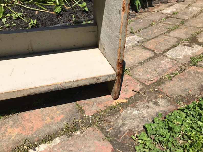 Pode incluir: Uma estante de madeira com acabamento pintado de branco. A estante &eacute; feita de madeira bruta e tem um visual r&uacute;stico. A estante est&aacute; sentada em um p&aacute;tio de tijolos.