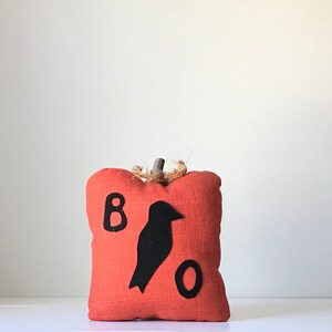 May include: A small orange fabric pumpkin with a black felt crow and the letters "BOO" on the front.