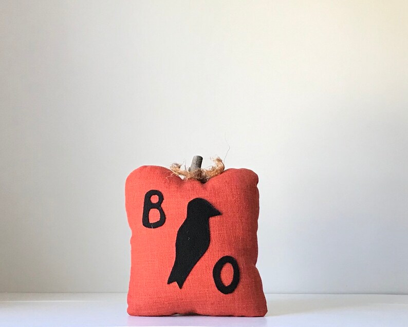 May include: A small orange fabric pumpkin with a black felt crow and the letters "BOO" on the front.