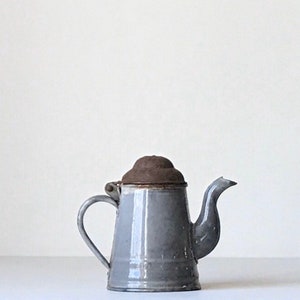 May include: A vintage gray metal teapot with a brown lid and a curved spout. The teapot has a handle and a small, round lid. The teapot is likely used for brewing tea or coffee.