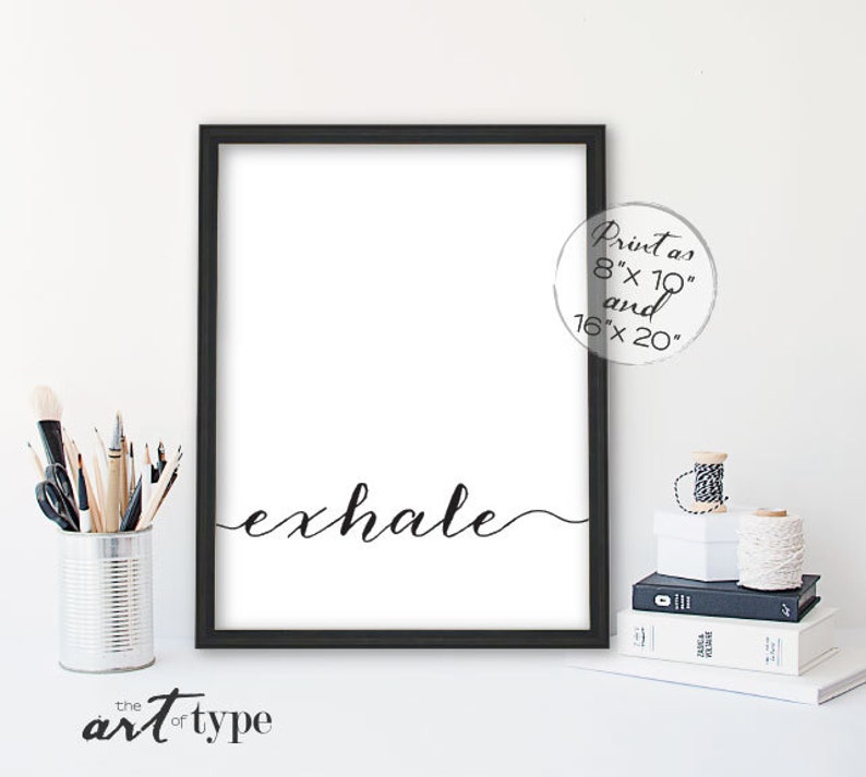 May include: A black framed art print featuring the word "exhale" in cursive. The print is on a white background and available in 20.3cm x 25.4cm and 40.6cm x 50.8cm sizes. The art is from "the art of type".