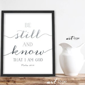 K&ouml;nnte beinhalten: Ein schwarzer gerahmter Druck mit wei&szlig;em Hintergrund und silbernen Buchstaben. Der Druck lautet "Be still and know that I am God, Psalm 46:10".