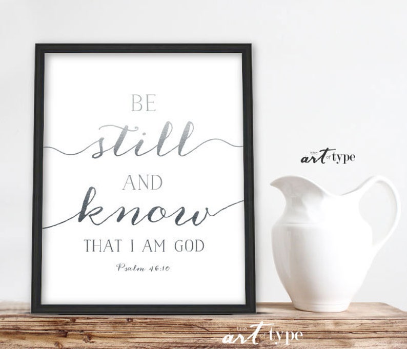K&ouml;nnte beinhalten: Ein schwarzer gerahmter Druck mit wei&szlig;em Hintergrund und silbernen Buchstaben. Der Druck lautet "Be still and know that I am God, Psalm 46:10".