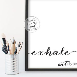 May include: A black framed print with the word "exhale" in elegant script. The phrase "the art of type" is below. A circular graphic indicates the print sizes are 20cm x 25cm and 40cm x 50cm. A metal container holds art supplies.