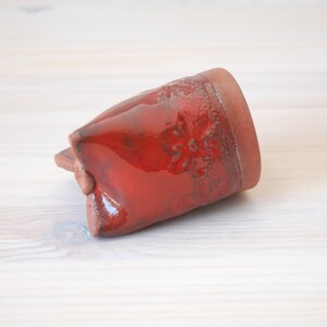 May include: A red ceramic mug with a textured surface. The mug is glazed and has a glossy finish.