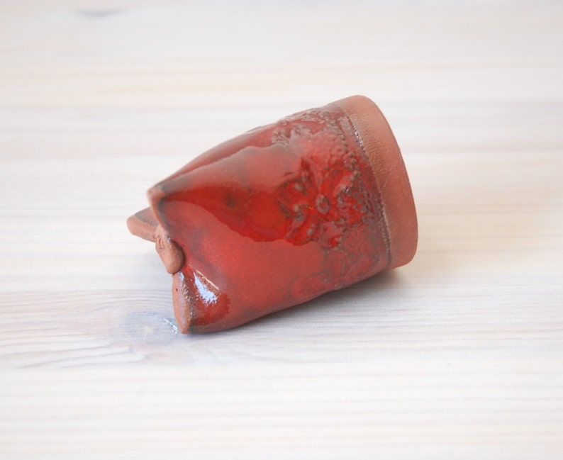 May include: A red ceramic mug with a textured surface. The mug is glazed and has a glossy finish.