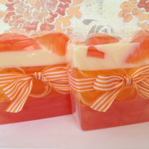 May include: Two rectangular bars of layered soap with orange, white, and pink colors. Each bar is tied with an orange and white striped ribbon.